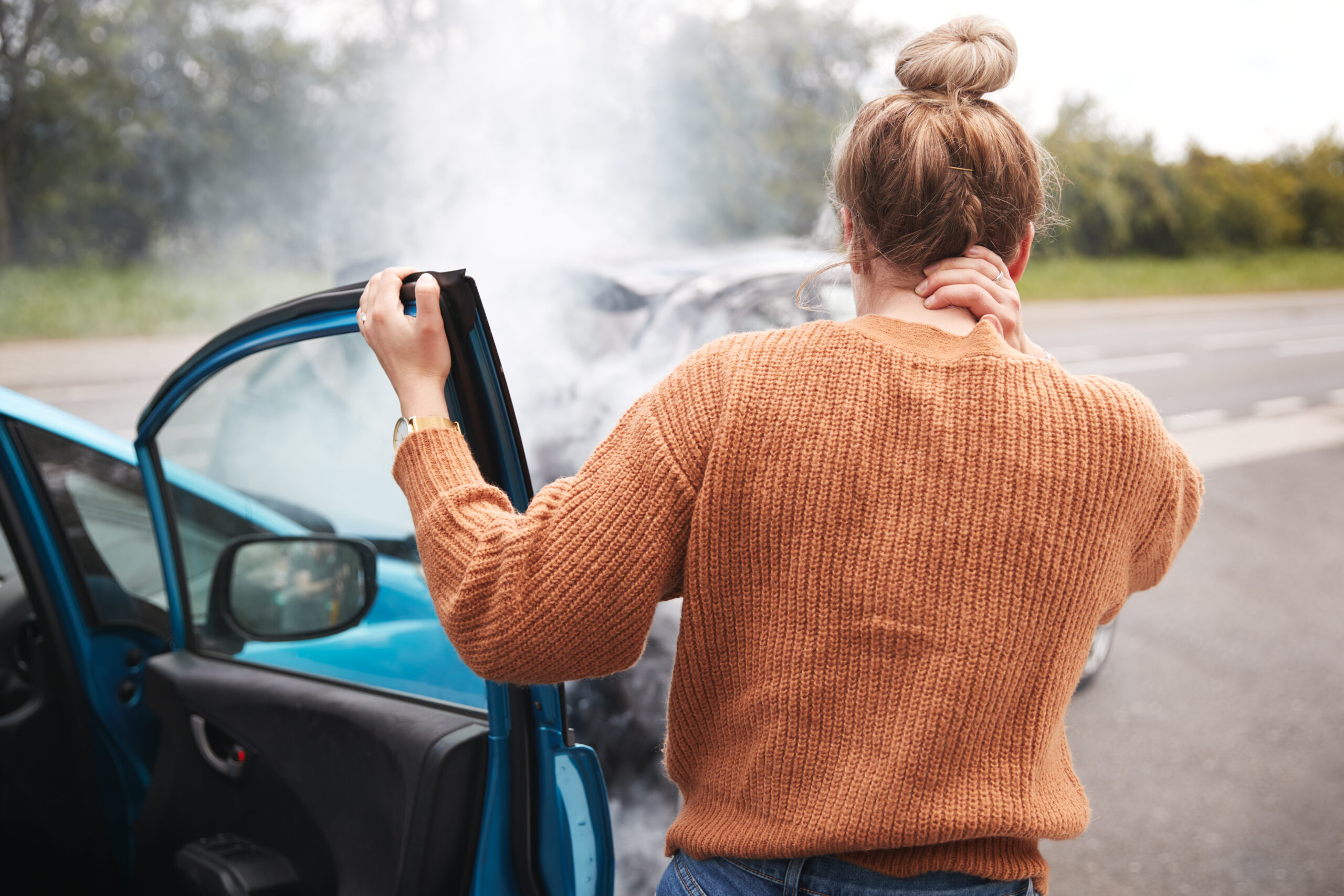 Car accident injury victim holding his neck beside an open car door after a collision