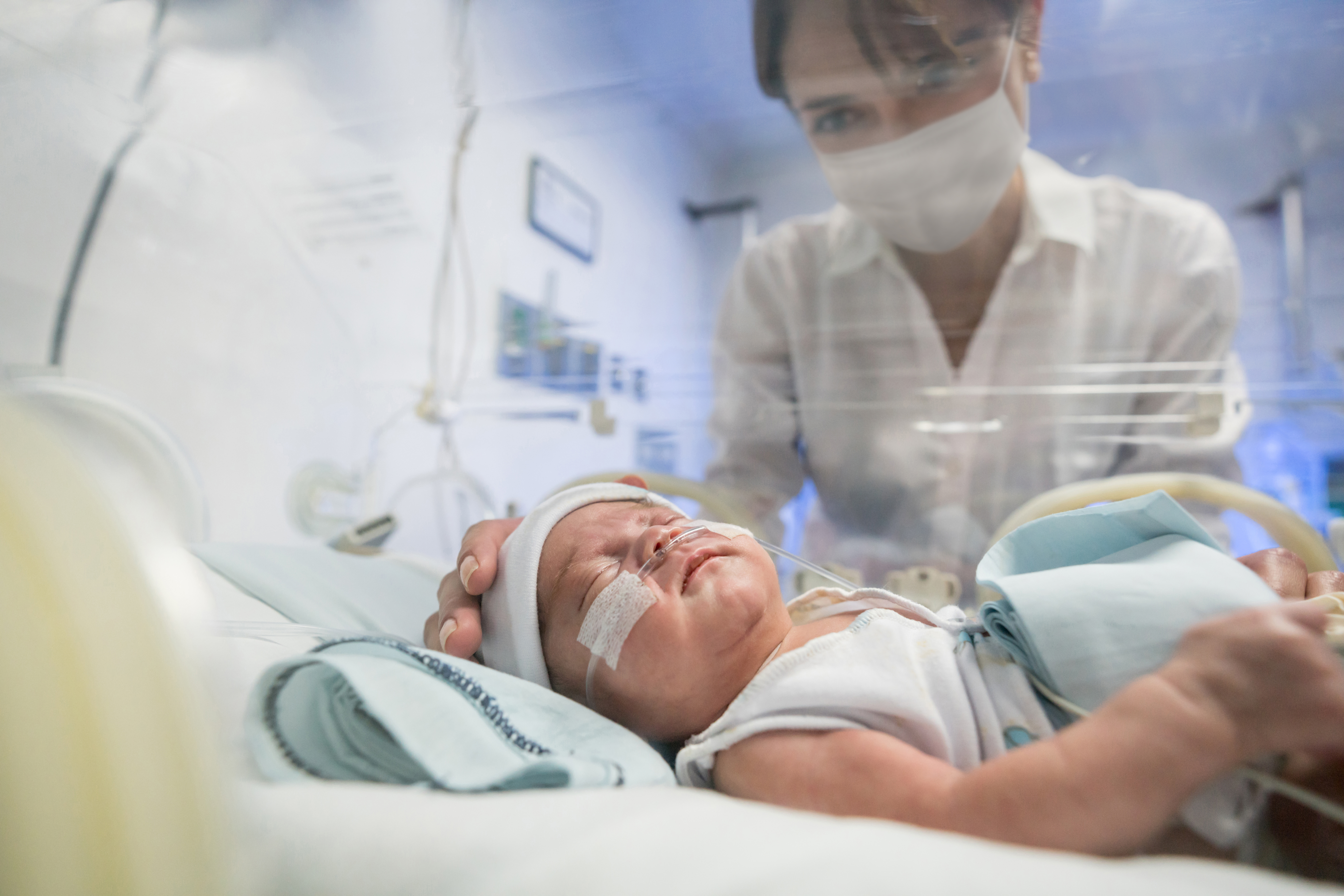 A nurse monitors a newborn baby receiving specialized medical care inside a hospital NICU incubator.